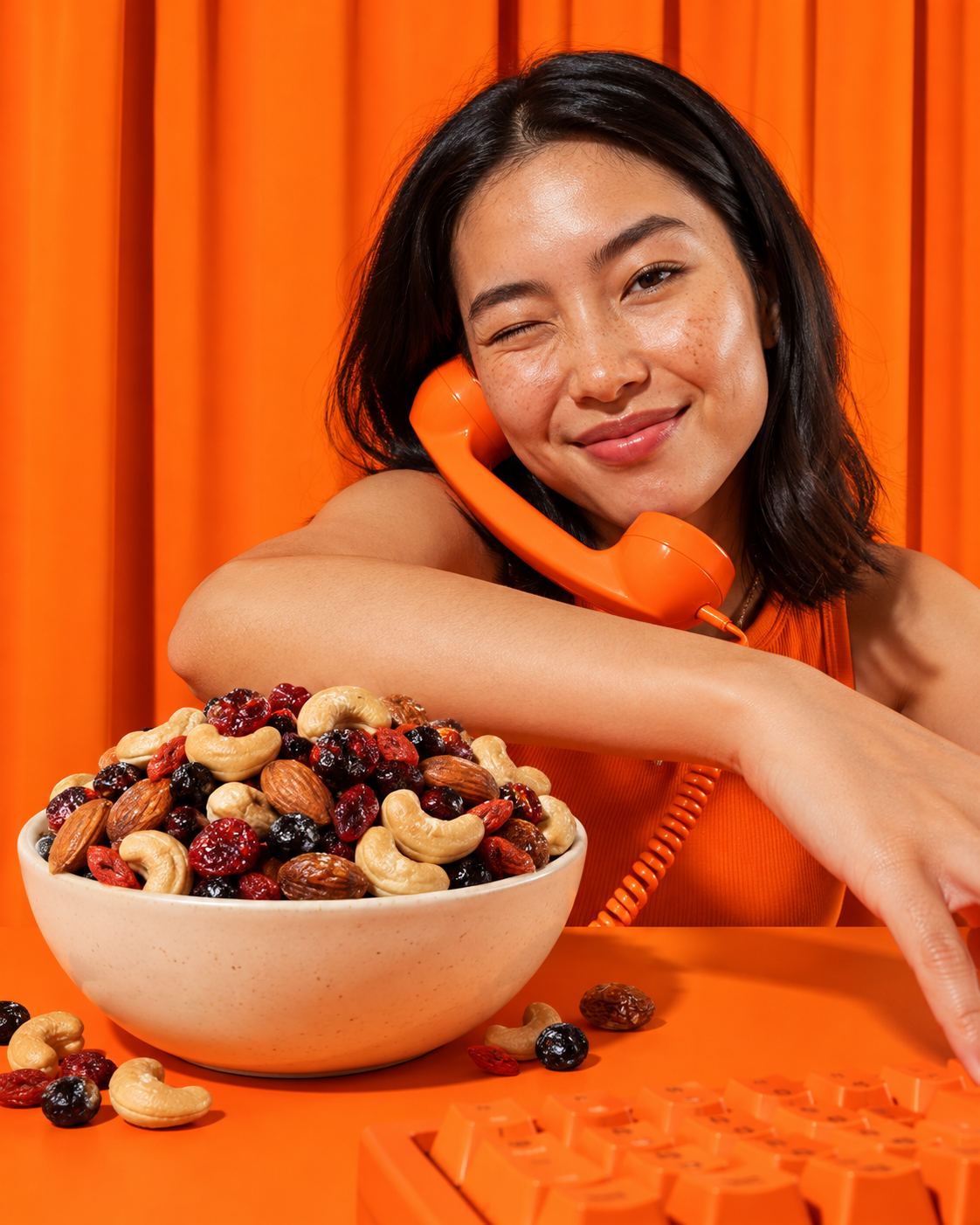 Woman holding an orange telephone beside a bowl of nuts and dried fruit